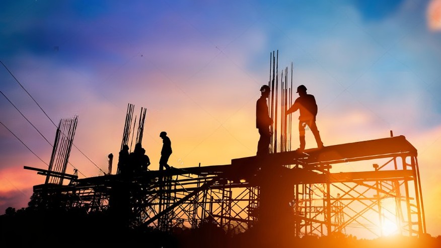 Siluetas de trabajadores de la construcción en andamios contra un cielo al atardecer, reflejando el costo de mano de obra en el presupuesto de construcción.