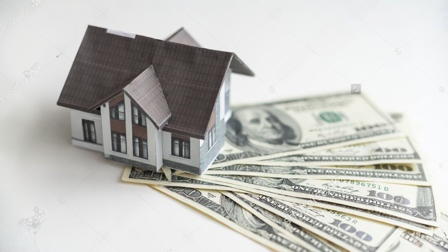 Modelo de casa sobre billetes de dólar representando el margen de seguridad en el presupuesto de construcción.